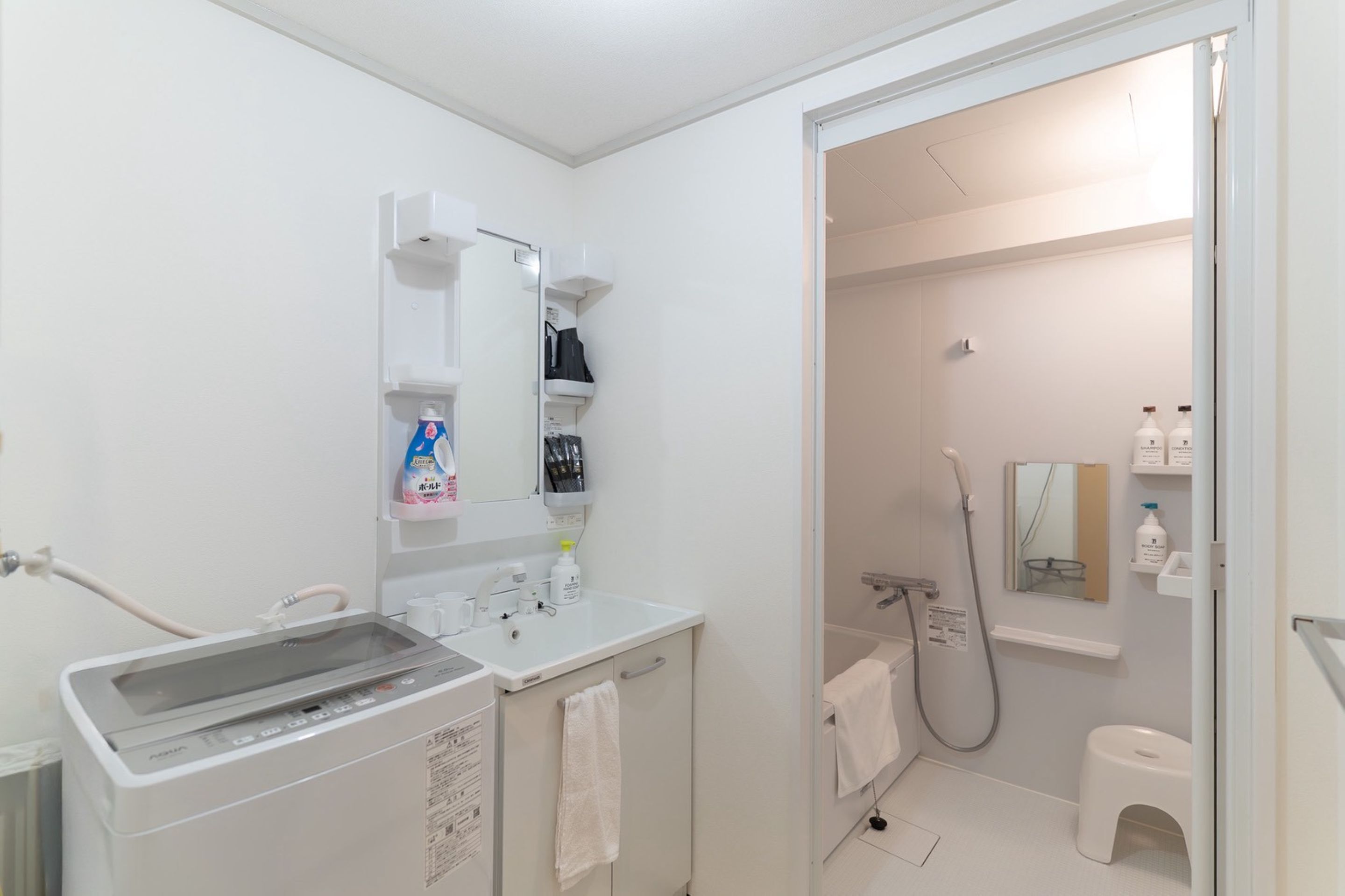 Een moderne badkamer met een ingebouwde wasmachine, een wastafel, een spiegel en een douchegedeelte.
