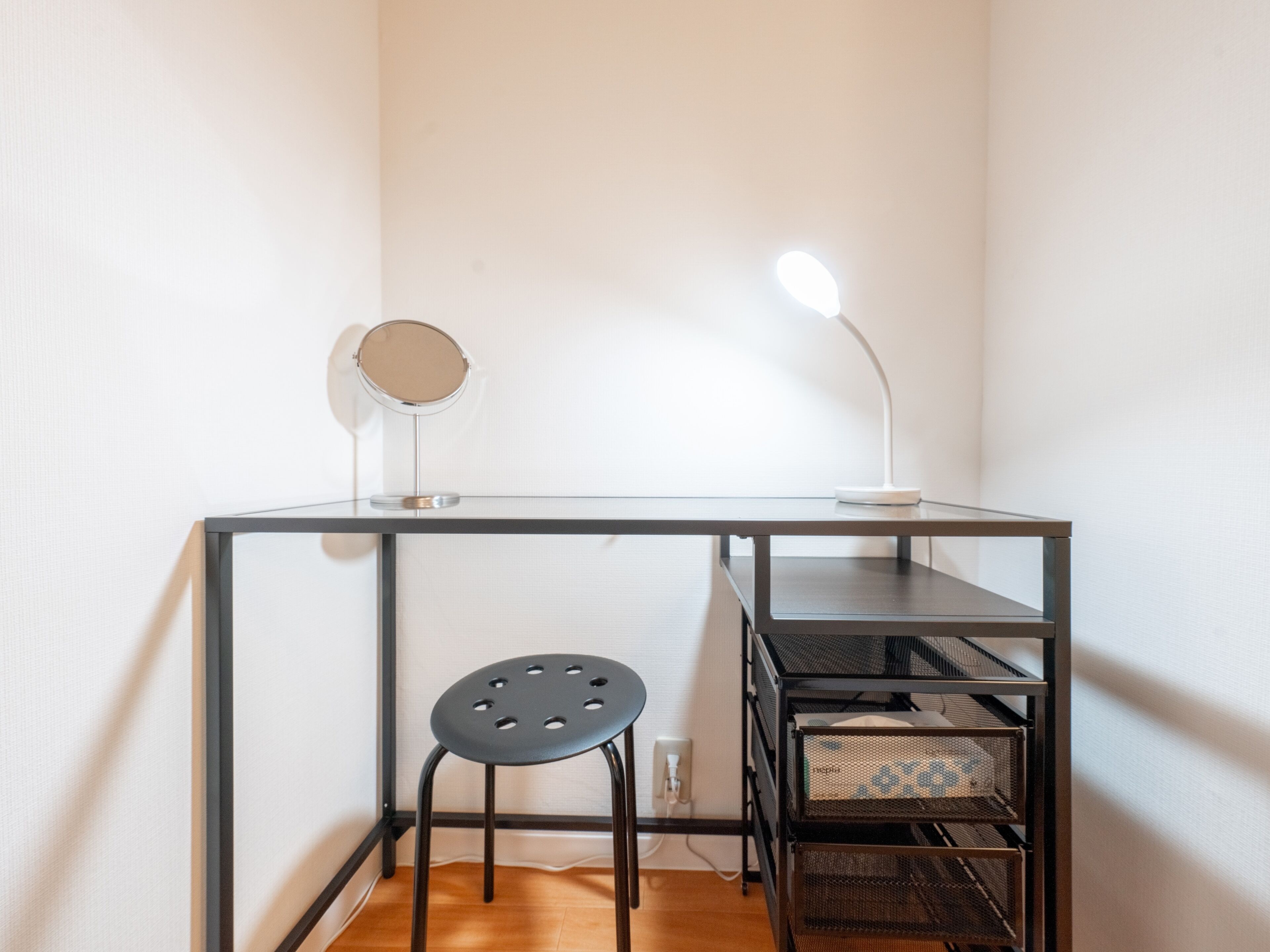 A workspace with a desk, two lamps, a stool, and storage boxes.