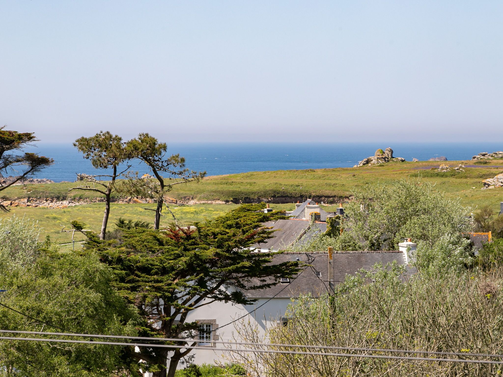 Paesaggio costiero con vista sul mare, una zona verdeggiante e un edificio con tetto a falde.