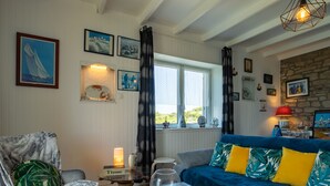 A cozy living room with a blue sofa, a chair with a leaf-patterned cushion, a glass coffee table, and a window with curtains. - La Grande Roche by Interhome (Porspoder)