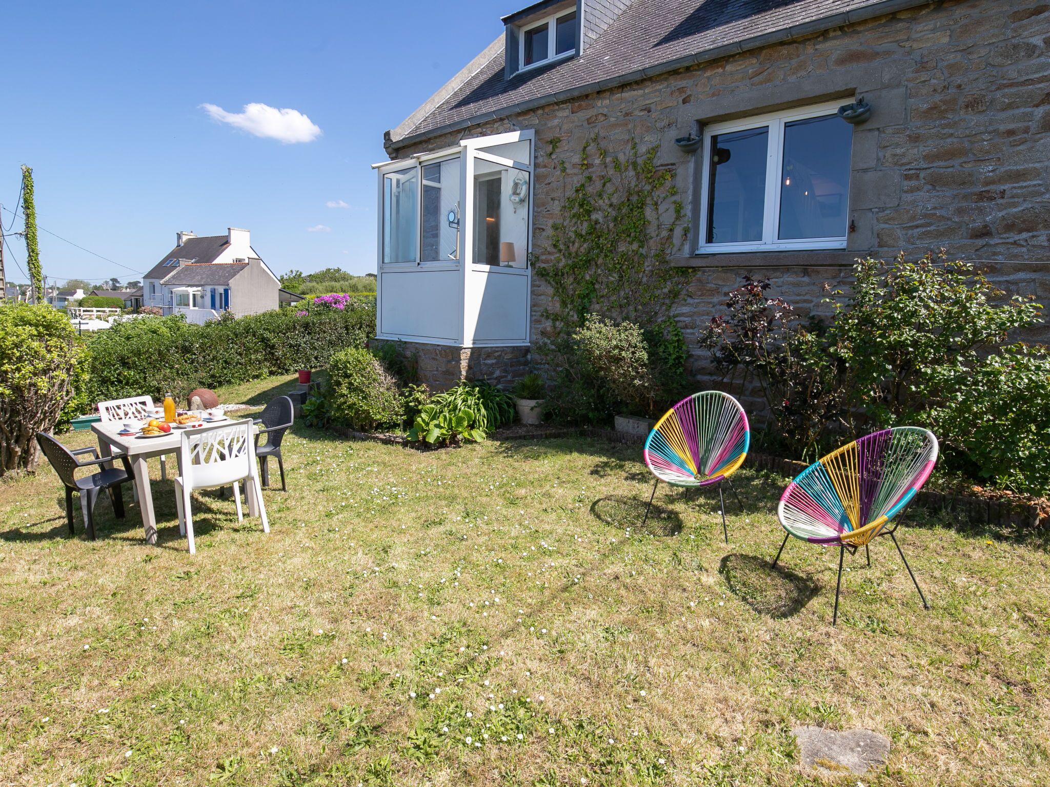 A stone house with a glass door, a table with chairs, and two colorful chairs in the yard.
