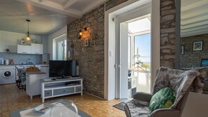 A modern living room with a stone wall, a television, a sofa, and a view of the outdoors. - La Grande Roche by Interhome (Porspoder)