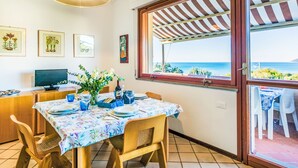 Uma área de refeições com uma mesa posta para dois, uma televisão e vista para o mar através de uma grande janela.