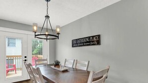 Un comedor con una mesa y sillas de madera, una araña y un letrero en la pared.