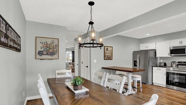 Una cocina moderna con armarios blancos, una mesa de comedor de madera y una araña.