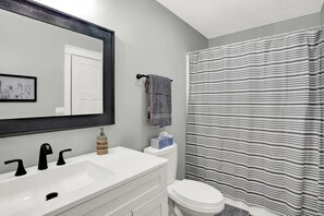 A bathroom with a white sink, black faucets, a toilet, and a striped shower curtain.