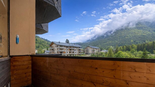 A wooden balcony with a view of a mountain and a building with multiple floors.