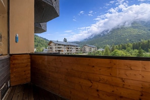 A wooden balcony with a view of a mountain and a building with multiple floors.