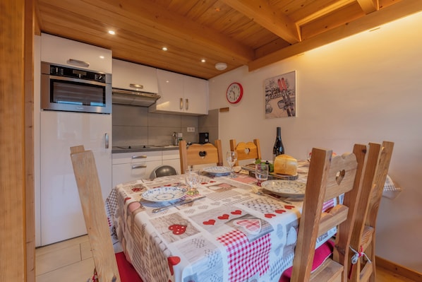 Una cocina acogedora con armarios de madera, horno empotrado y comedor con mesa para dos.