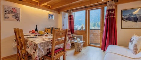 A cozy room with wooden beams, a dining area with a table set for two, and a bed with a mountain view.