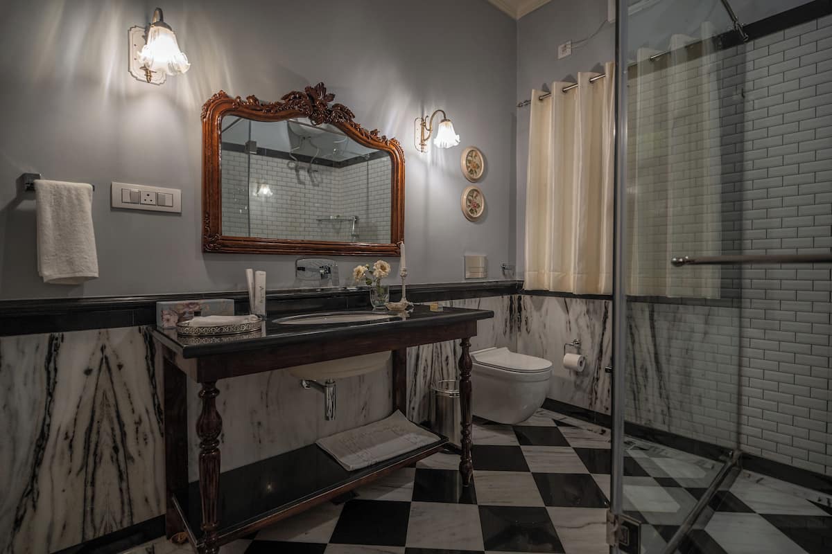 Un baño con piso a cuadros blanco y negro, un lavamanos de mármol, un espejo grande y una cabina de ducha de vidrio.