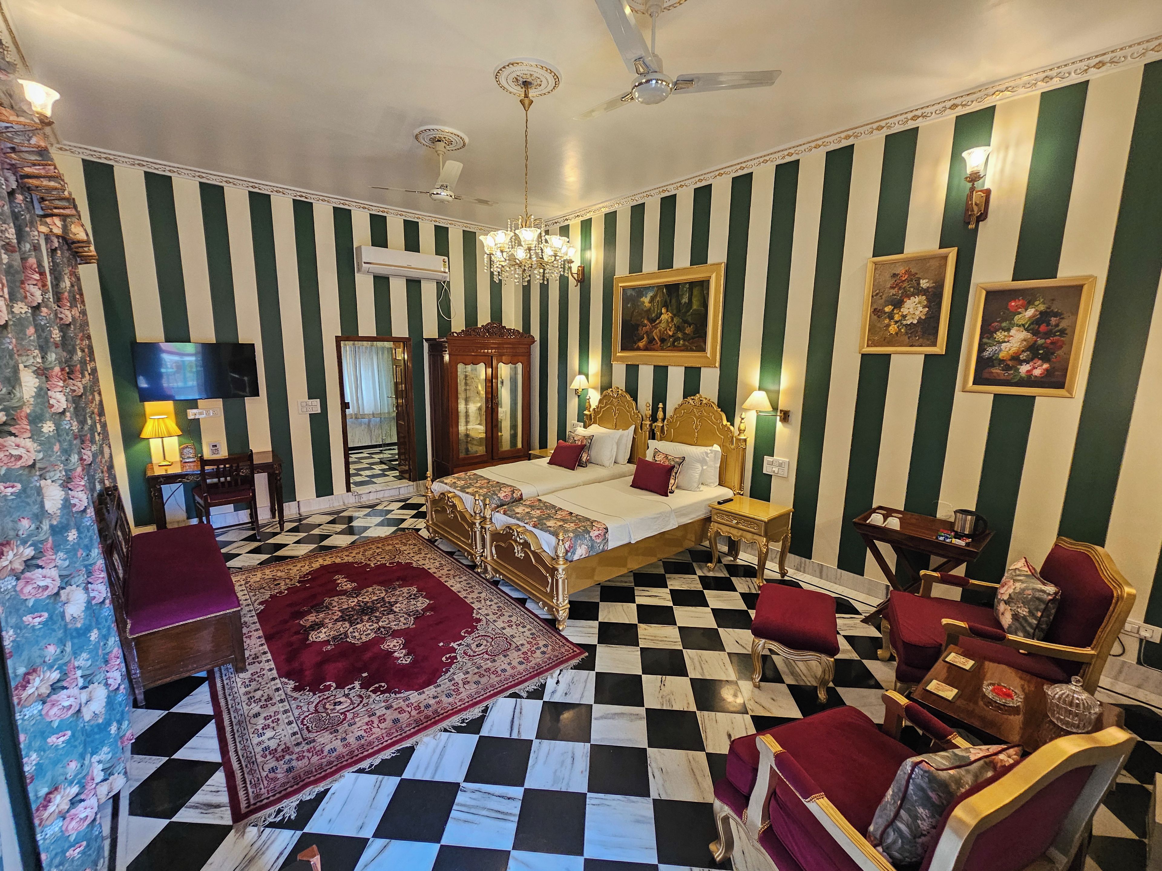 Una habitación de hotel con piso a cuadros, dos camas con cabeceros ornamentados, un candelabro y un espejo grande.