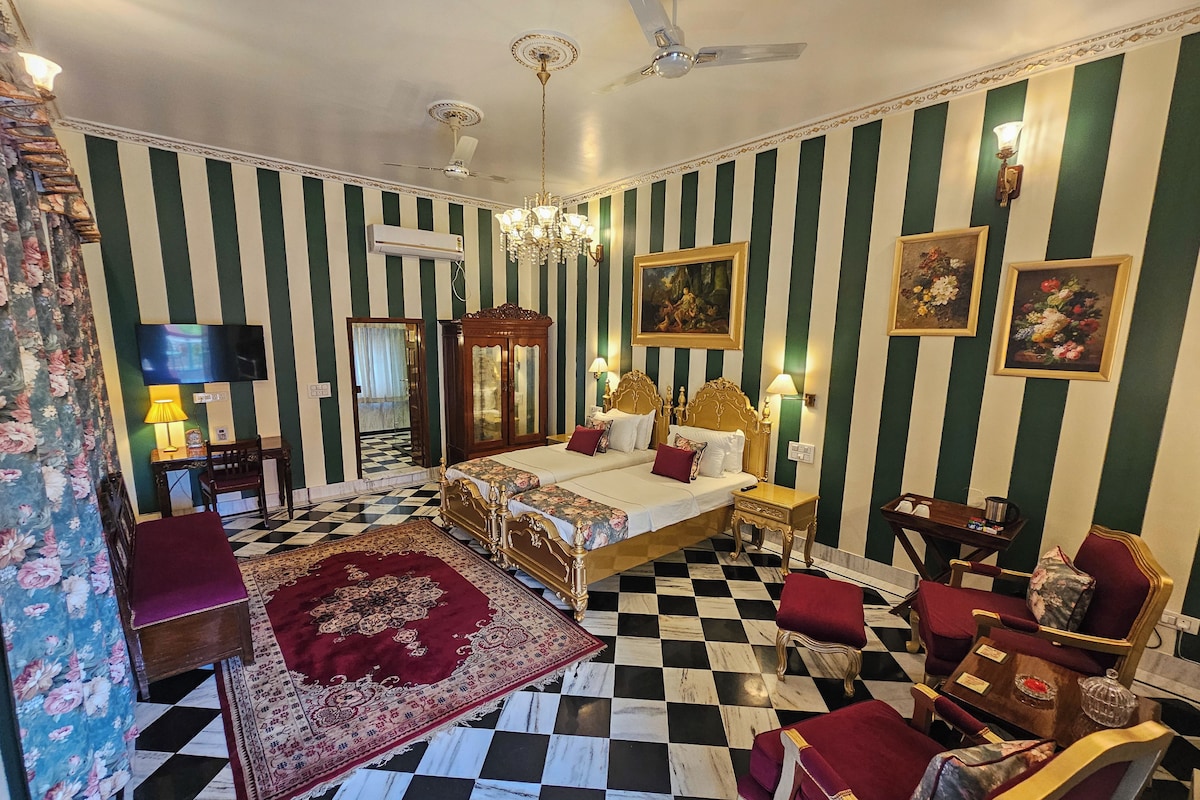 Una habitació d'hotel amb un terra de pissos de quadres, dos llits amb els capços decorats, un penjallum i un mirall gran.
