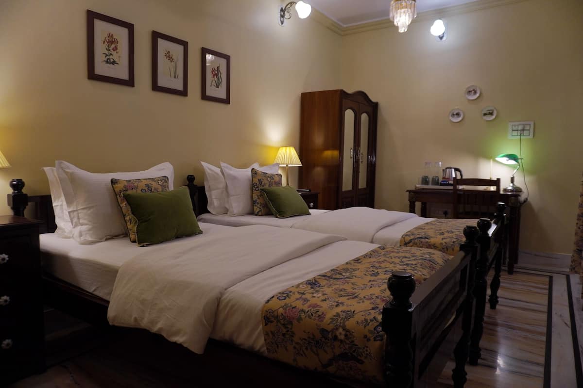 Habitación de hotel con dos camas, un armario de madera, un escritorio con lámpara y cuadros en la pared.