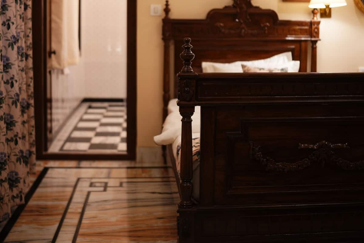 Un dormitorio con cama de madera, una mesita de noche con lámpara, un cuadro enmarcado en la pared y suelo a cuadros.