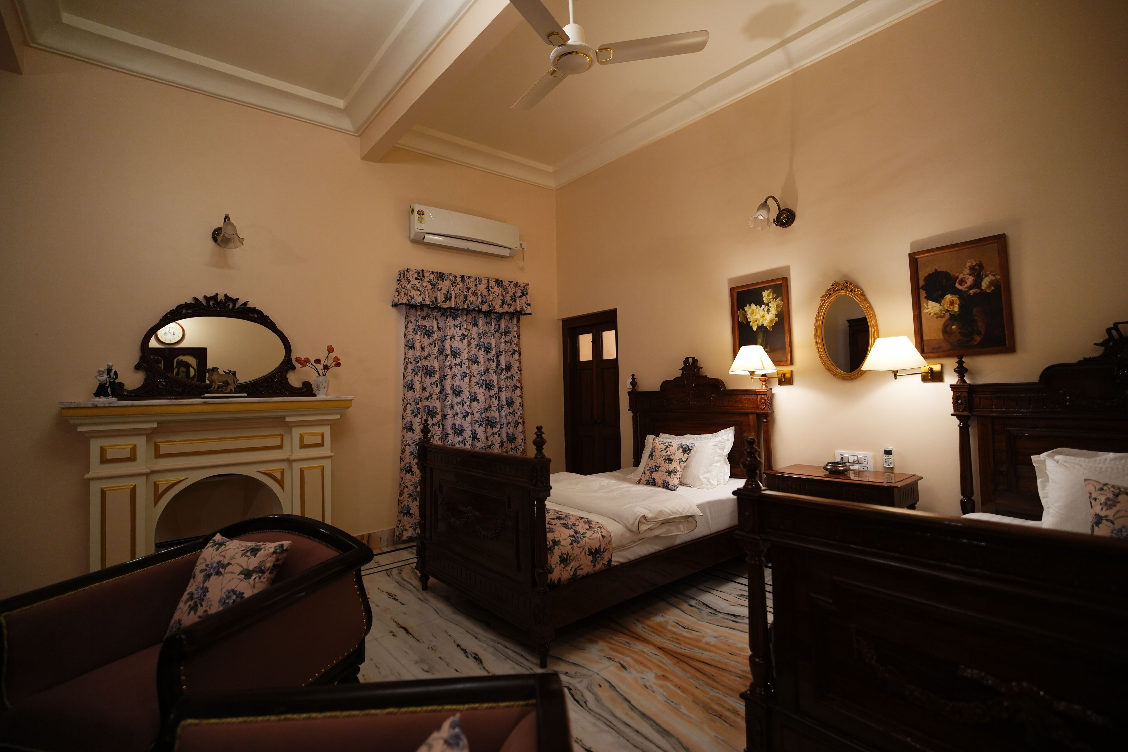 Habitación de hotel con cama, sillón, tocador con espejo, chimenea y ventilador de techo.