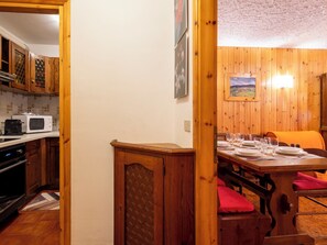 A wooden interior with a dining table set for four, a kitchen with a microwave, and wooden cabinets. - Casa Rossa by Interhome (Madesimo)