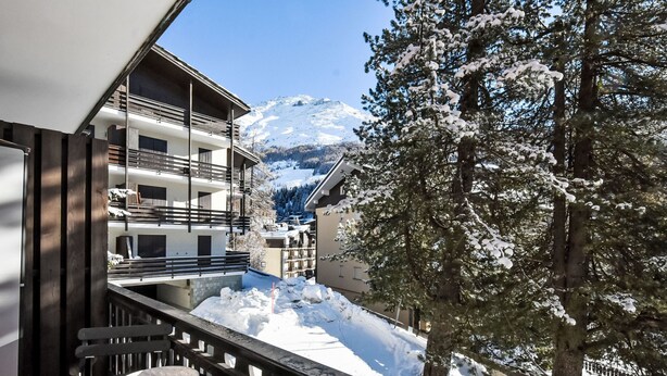 A balcony with a table and chairs, overlooking a snowy mountain and a tree. - Casa Rossa by Interhome (Madesimo)