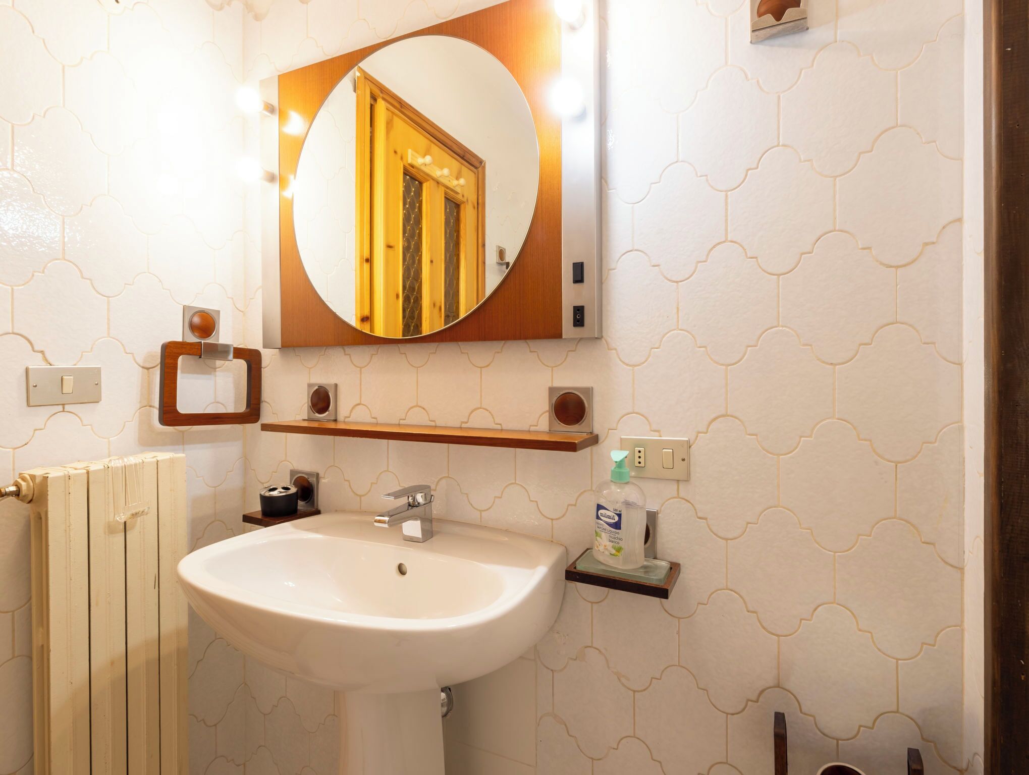 A bathroom with a white sink, a mirror, a wooden door, and a towel rack.