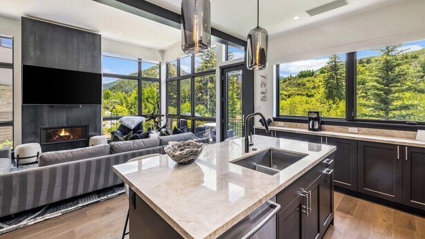 A modern kitchen with a large island, dark cabinetry, and a fireplace.