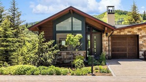 A modern house with a large garage, surrounded by a well-maintained garden and a mountain backdrop.