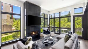 A modern living room with a fireplace, large windows, and a view of greenery.