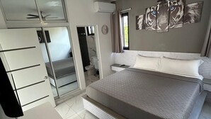 Egy modern hálószoba, amelyben egy nagy ágy, egy mennyezeti ventilátor, egy fürdőszoba és egy gardróbszekrény található.