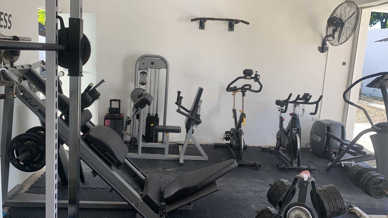 A gym with various exercise equipment including a bench press, dumbbells, a stationary bike, and a treadmill.