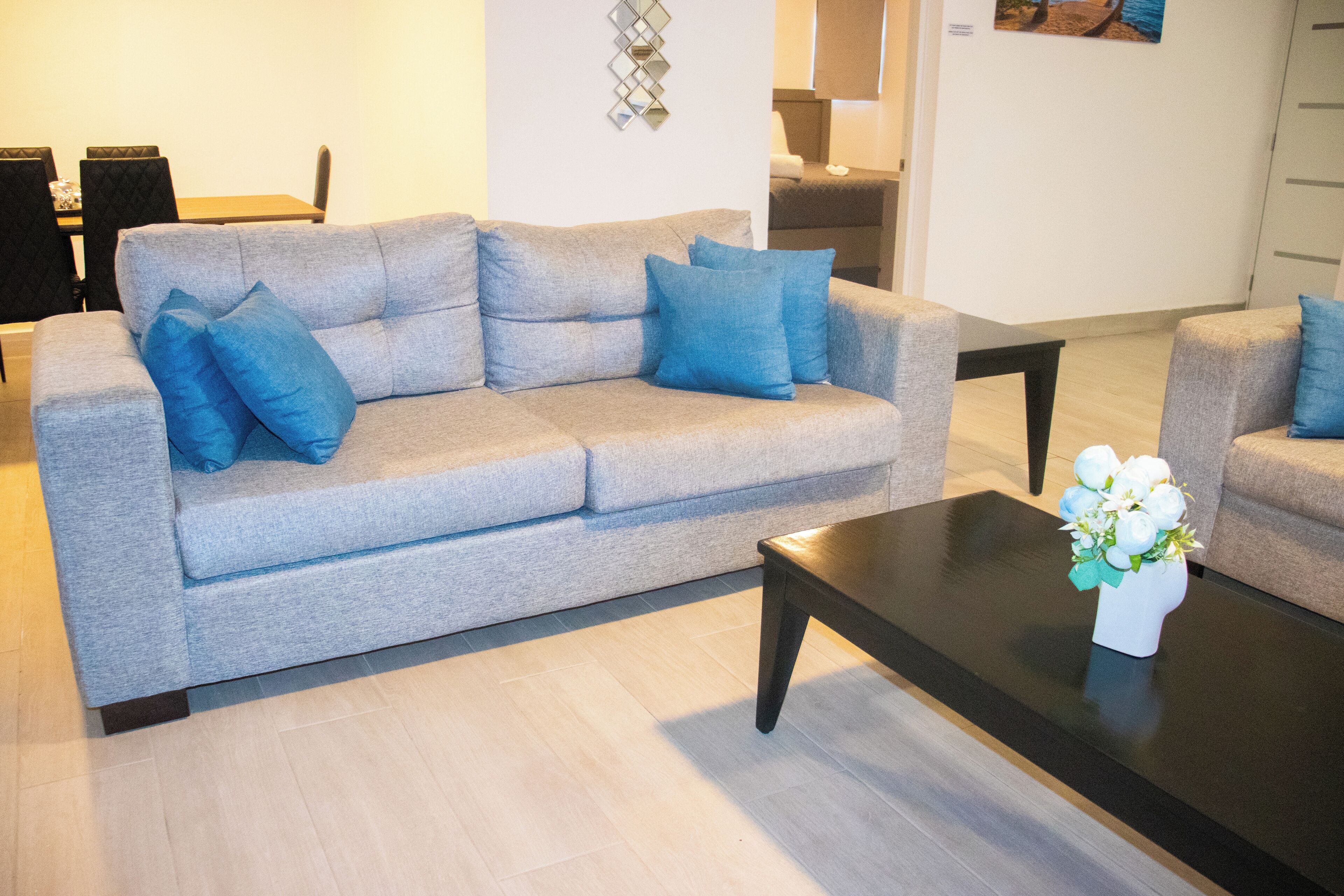 A modern living room with a grey sofa, blue cushions, a black coffee table, and a white vase with flowers.
