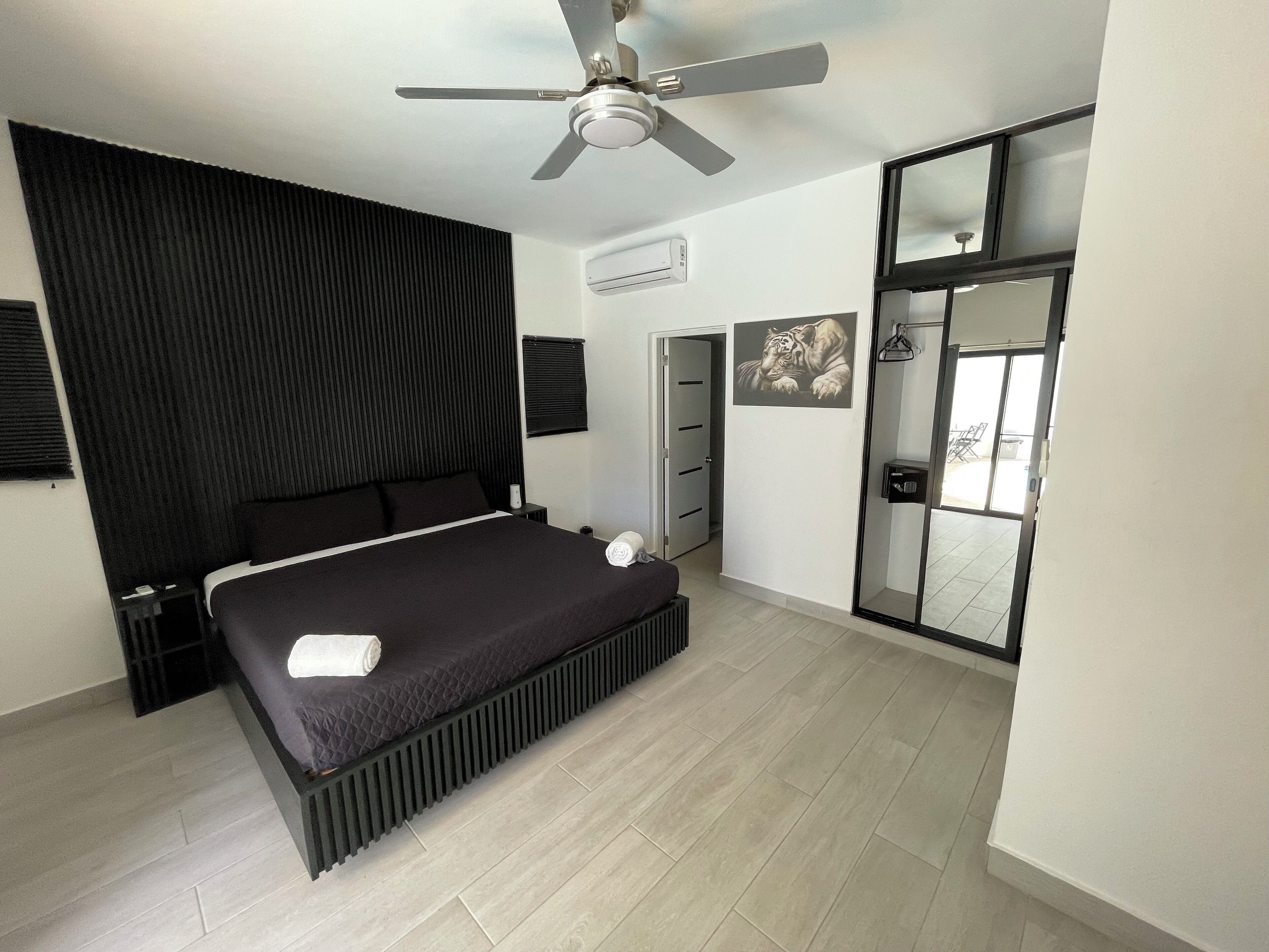 Un dormitorio moderno con una cama grande, un ventilador de techo, una puerta corrediza de vidrio y un aire acondicionado de pared.