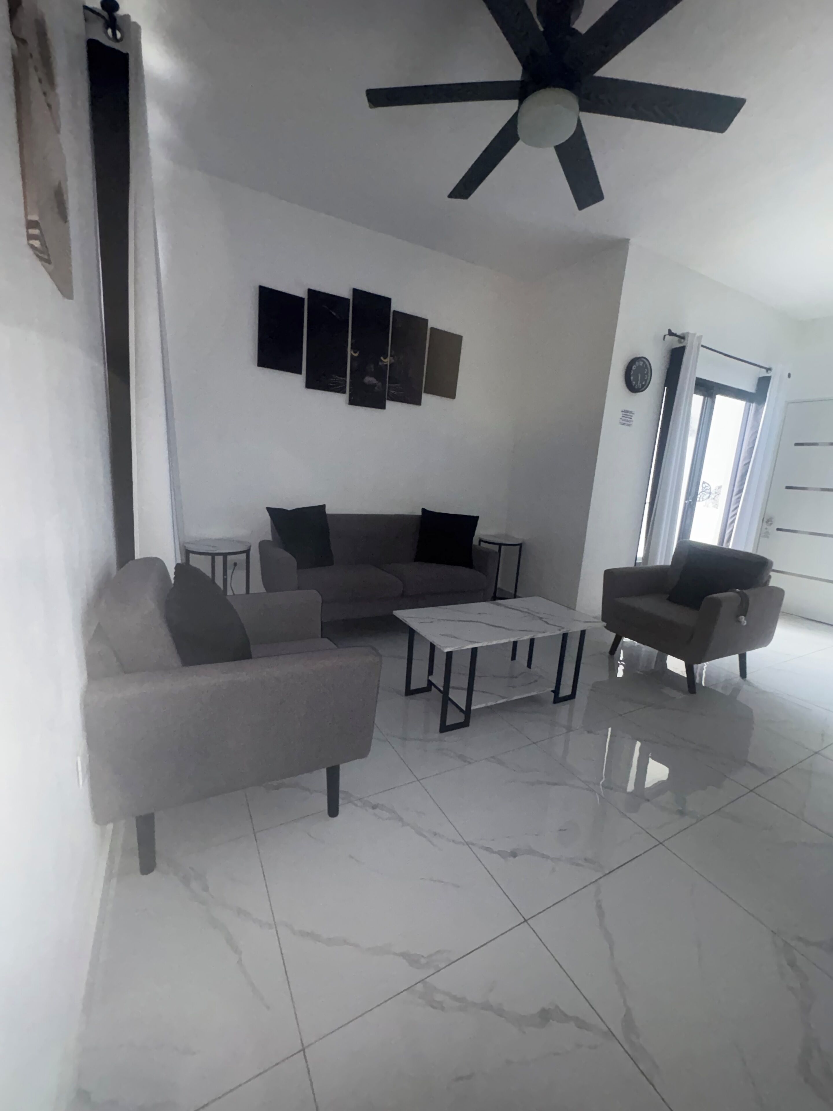 A modern living room with a sofa, armchairs, a coffee table, and a ceiling fan.