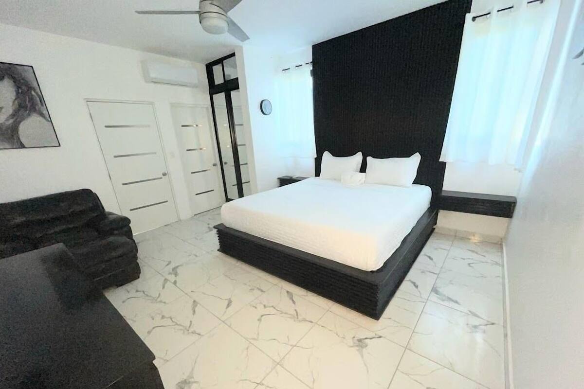 Un dormitorio moderno con una cama grande, un ventilador de techo, un cabecero oscuro y un suelo de mármol.