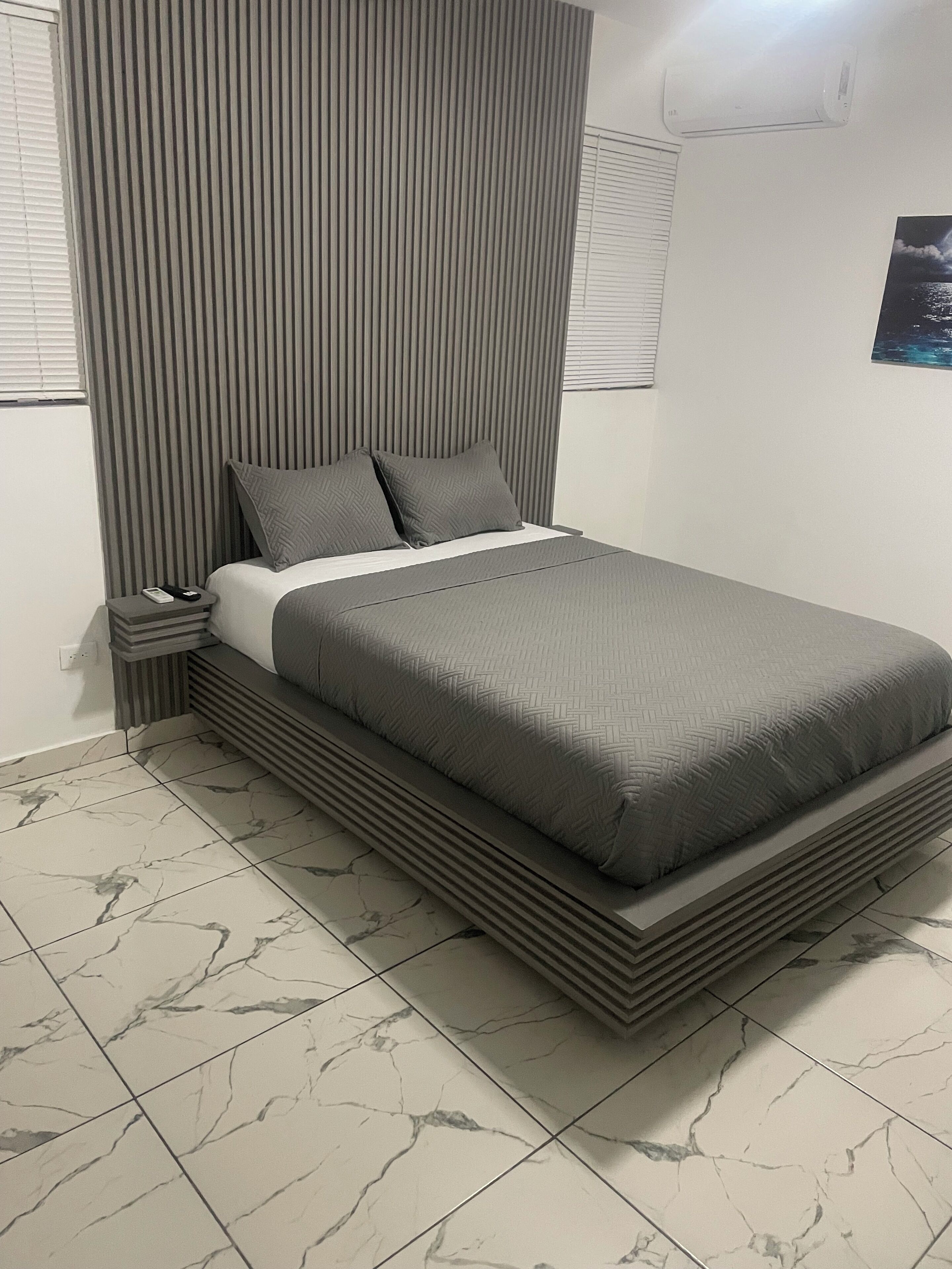 Un dormitorio moderno con cama, mesita de noche y aire acondicionado instalado en la pared.