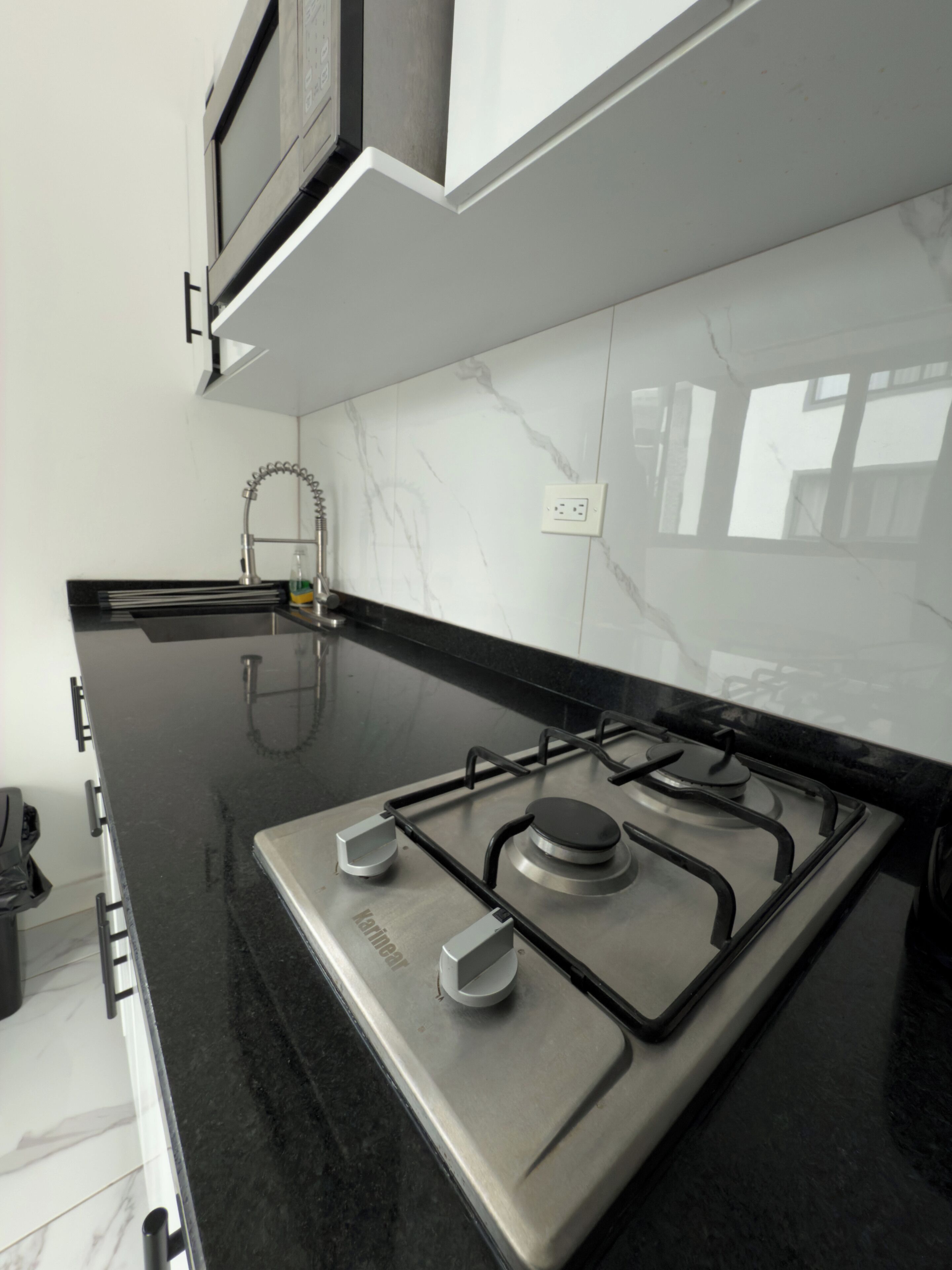 A modern kitchen with a stainless steel gas stove, black countertops, white marble backsplash, and white cabinets.