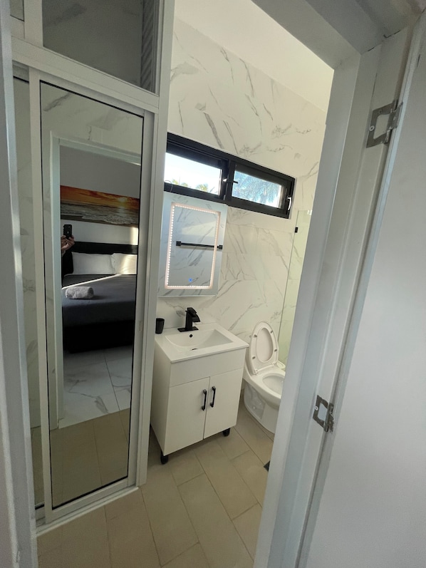 A modern bathroom with a white marble wall, a built-in sink, a toilet, and a glass shower enclosure.