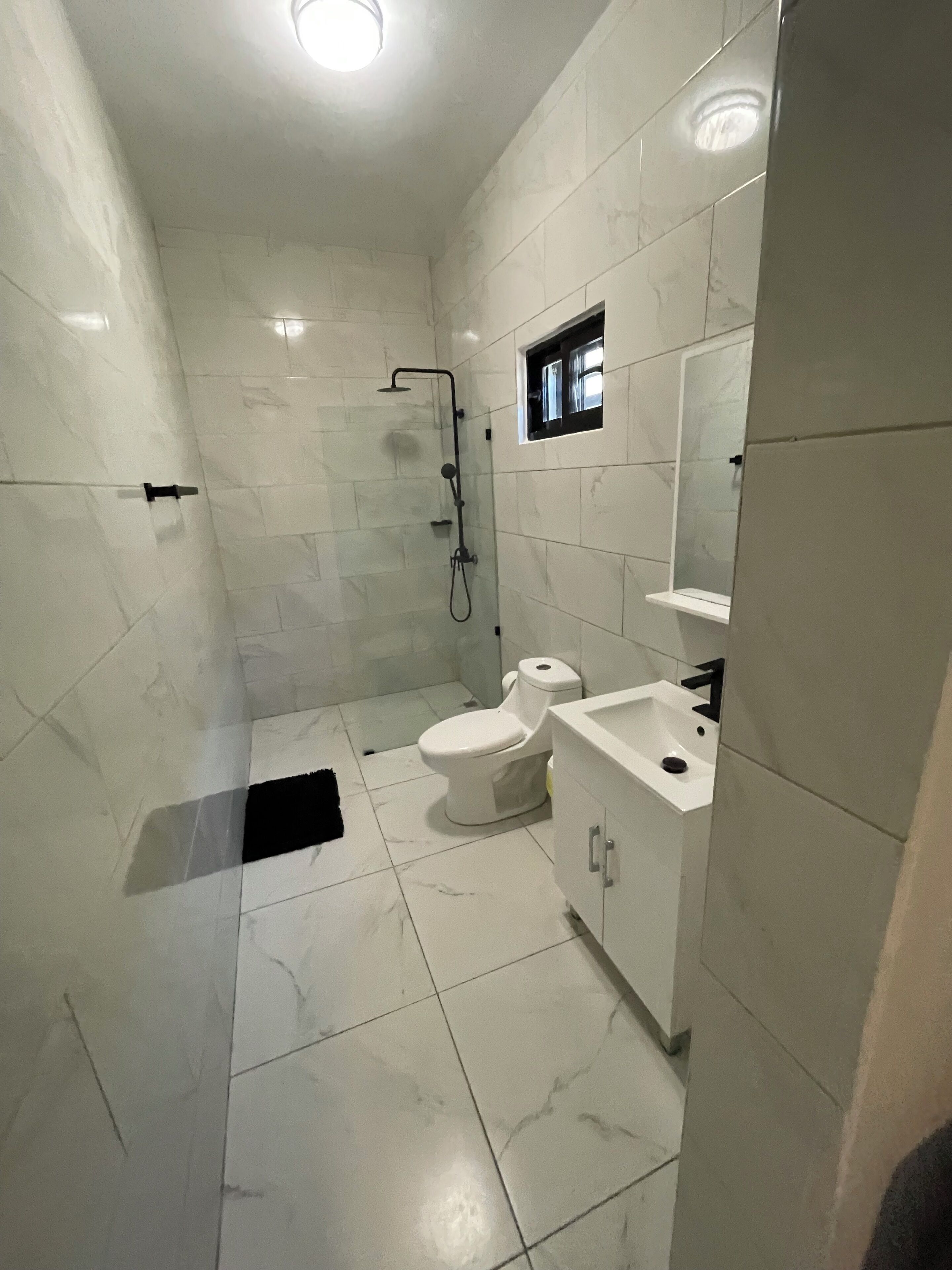 Et badeværelse med hvide marmorfliser, toilet, håndvask og bruser.