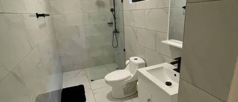 Et badeværelse med hvide marmorfliser, toilet, håndvask og bruser.