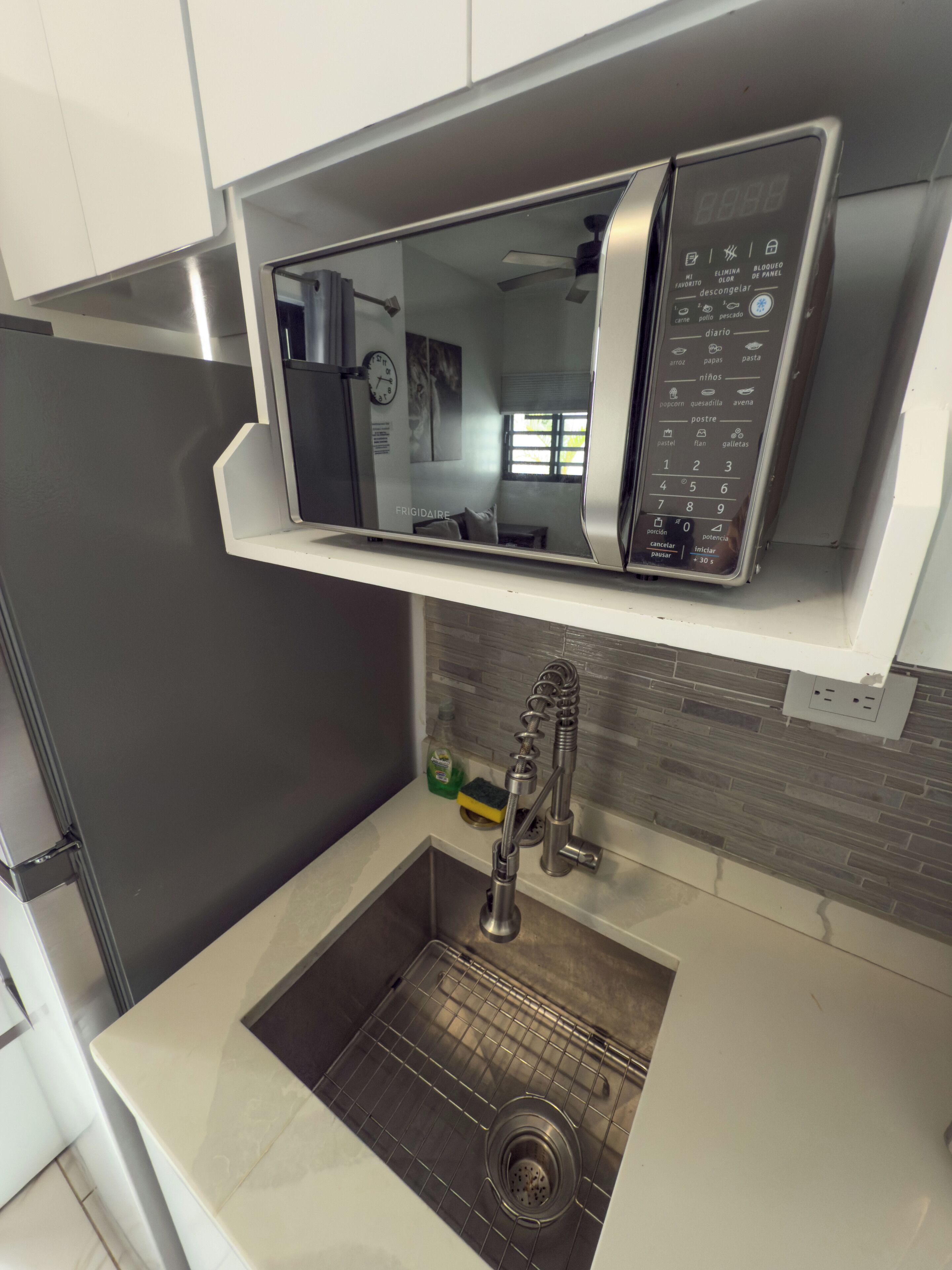 Een keuken met een roestvrijstalen koelkast, een magnetron en een spoelbak met een moderne kraan.