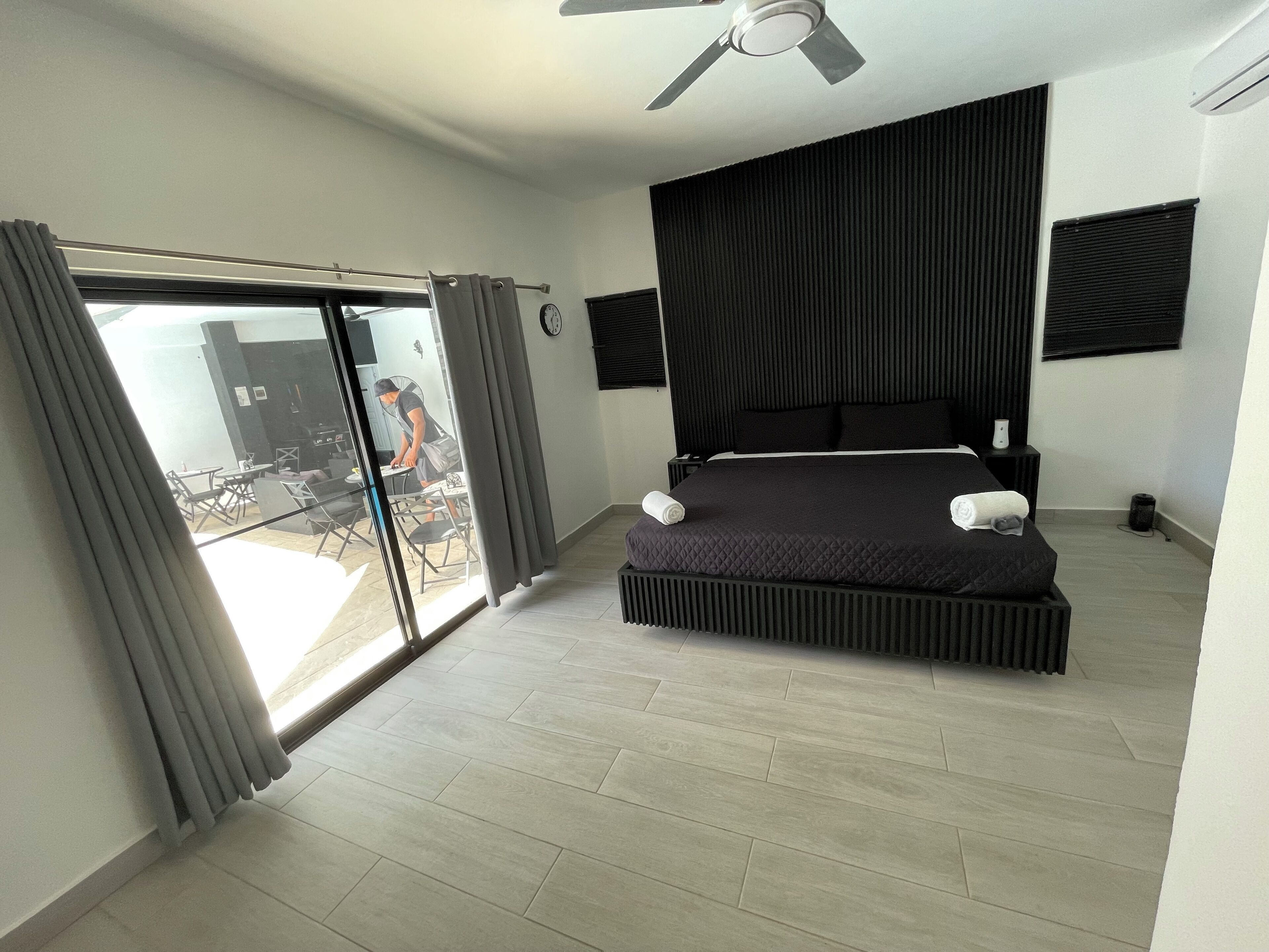 A modern bedroom with a large bed, a ceiling fan, and a sliding glass door leading to an outdoor area.
