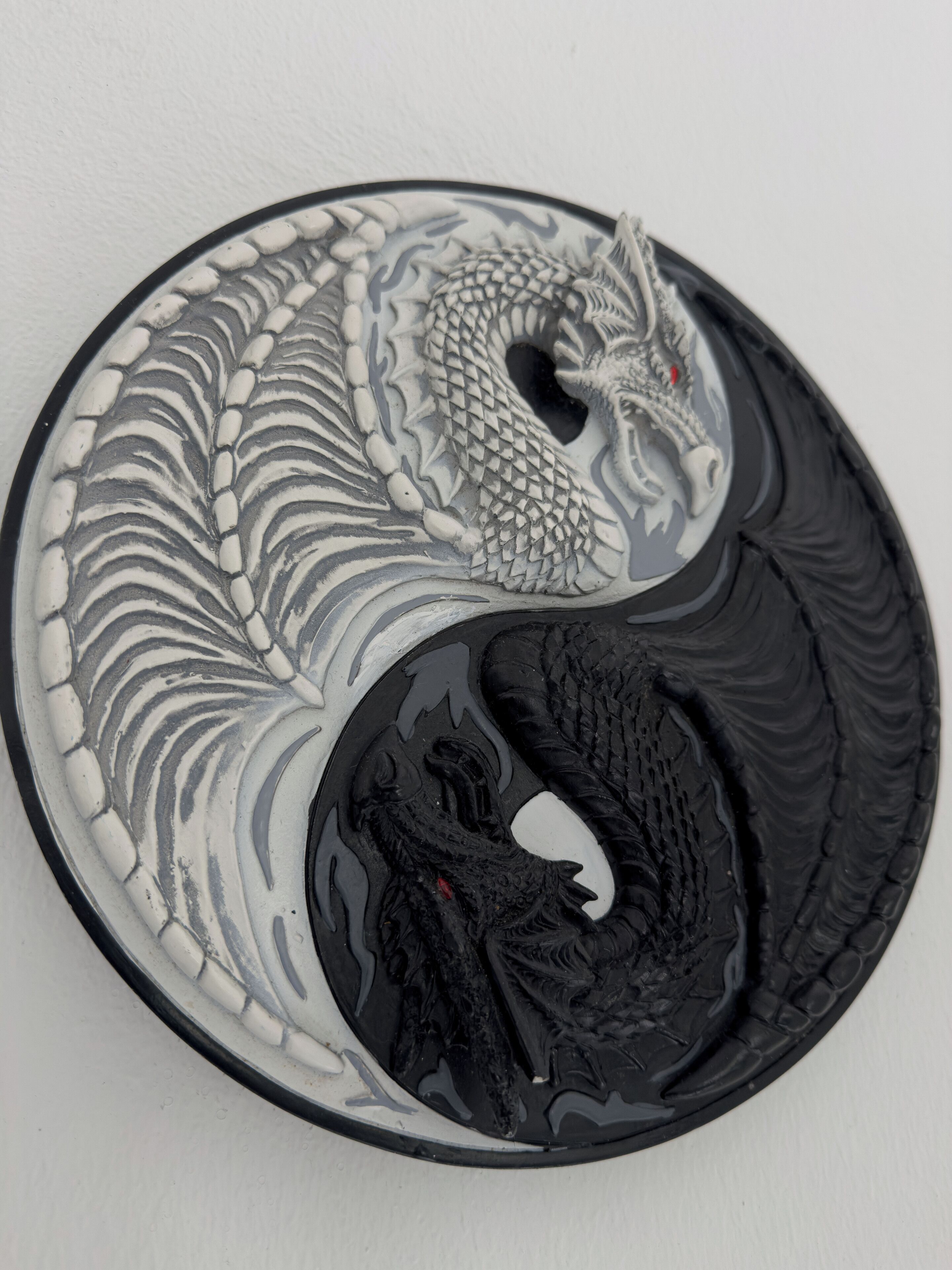 Un objet circulaire orné d’un motif de dragon, divisé en deux moitiés aux couleurs contrastées.