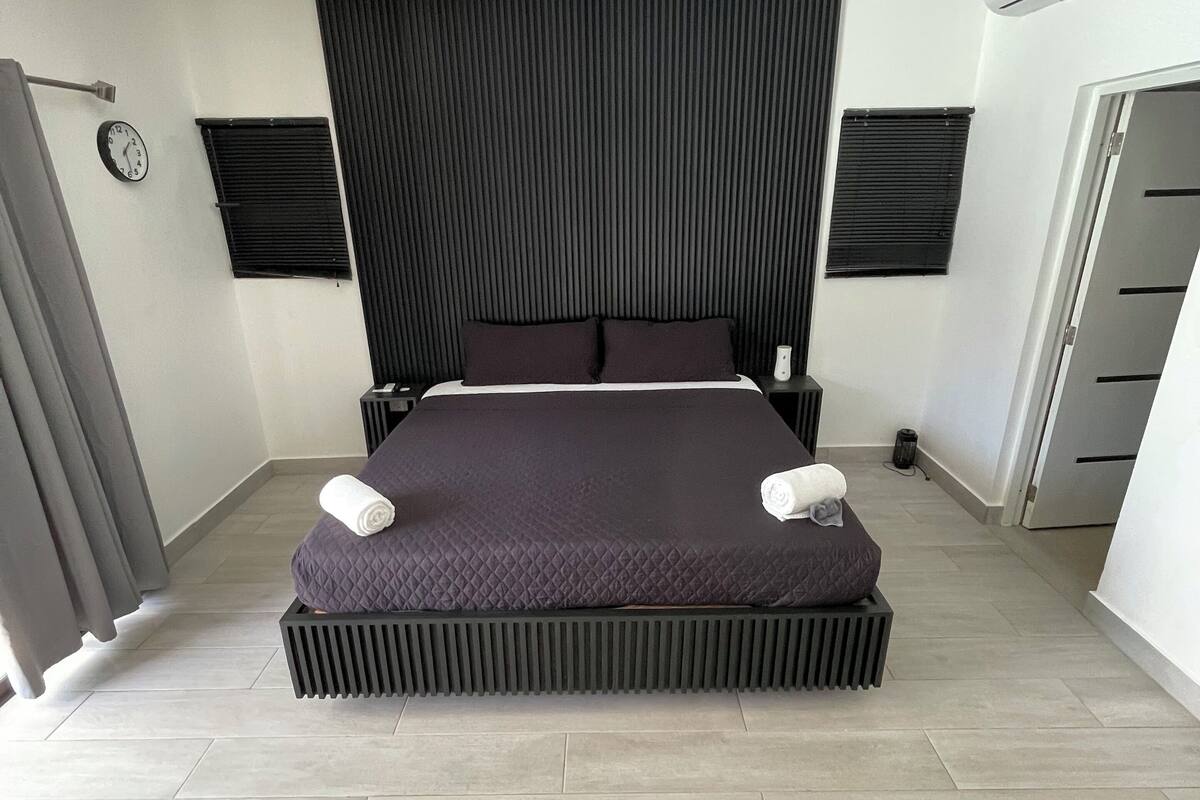 Un dormitorio moderno con cama, ventilador de techo, reloj y aire acondicionado.