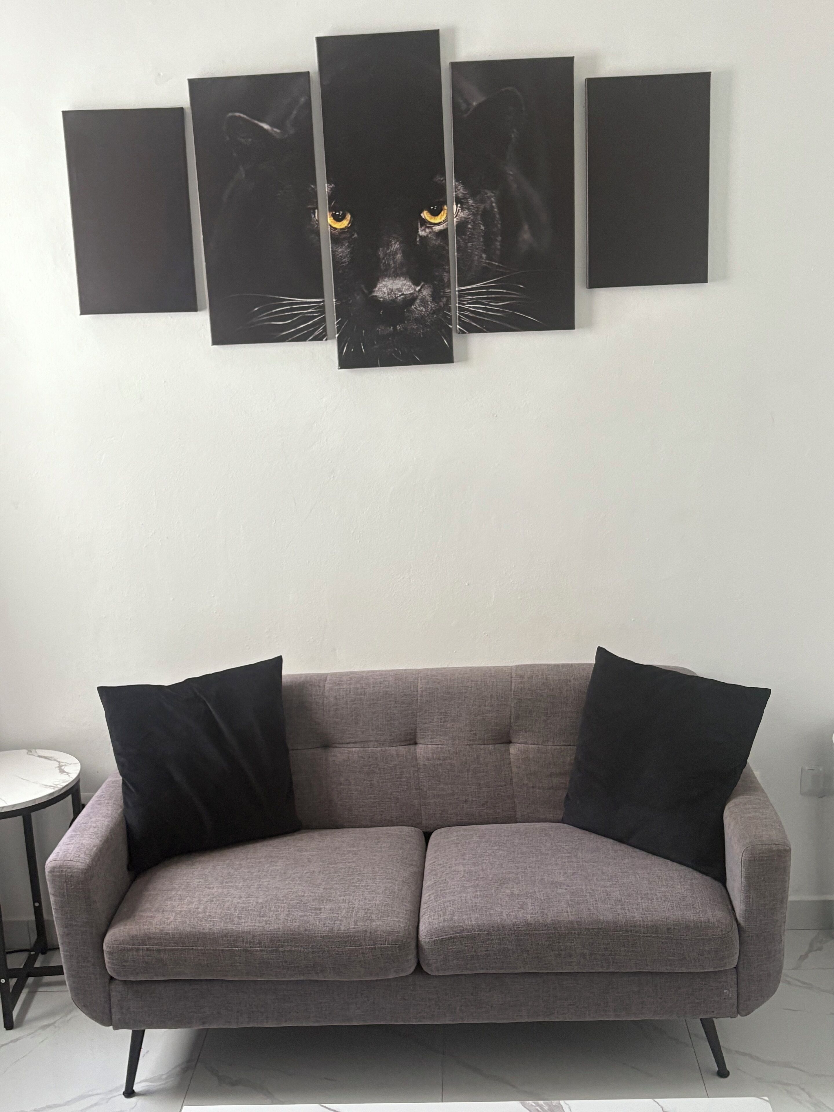 A grey sofa with black cushions in a room with a white wall.
