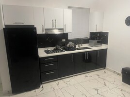 Una cocina con gabinetes negros, encimera blanca, estufa, pileta y microondas.