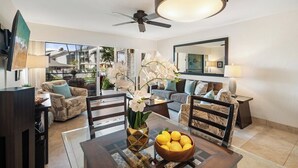 A modern living room with a dining area, featuring a ceiling fan, a large mirror, and a view of the outdoors.