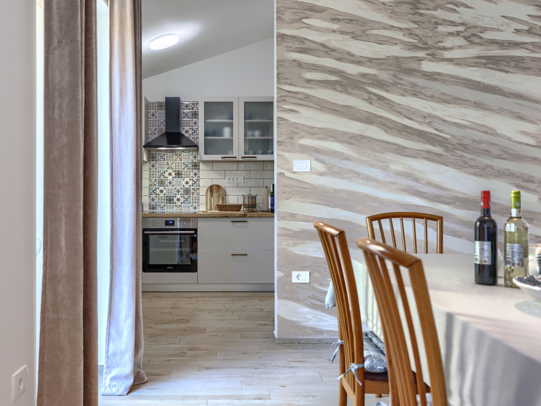 A modern kitchen with a built-in oven, a patterned backsplash, and a dining area with a marble table and chairs.