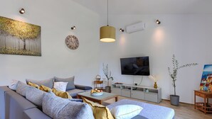 En moderne stue med sofa, fjernsyn, kunst og dekorativ belysning.