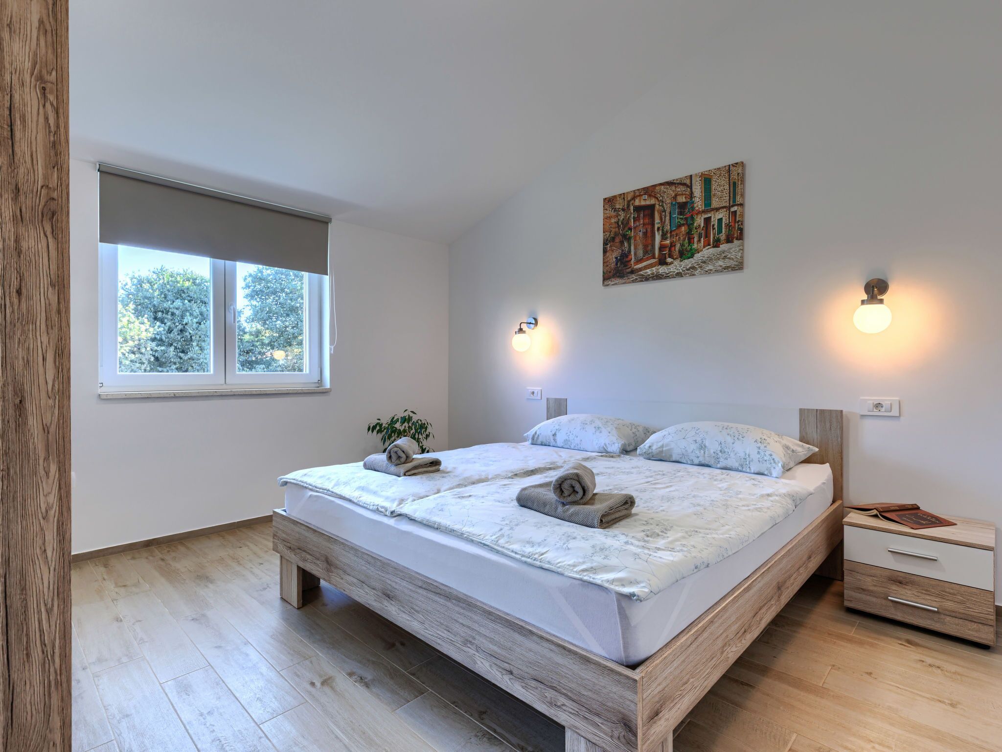 A bedroom with a bed, bedside tables, a window, and a painting on the wall.