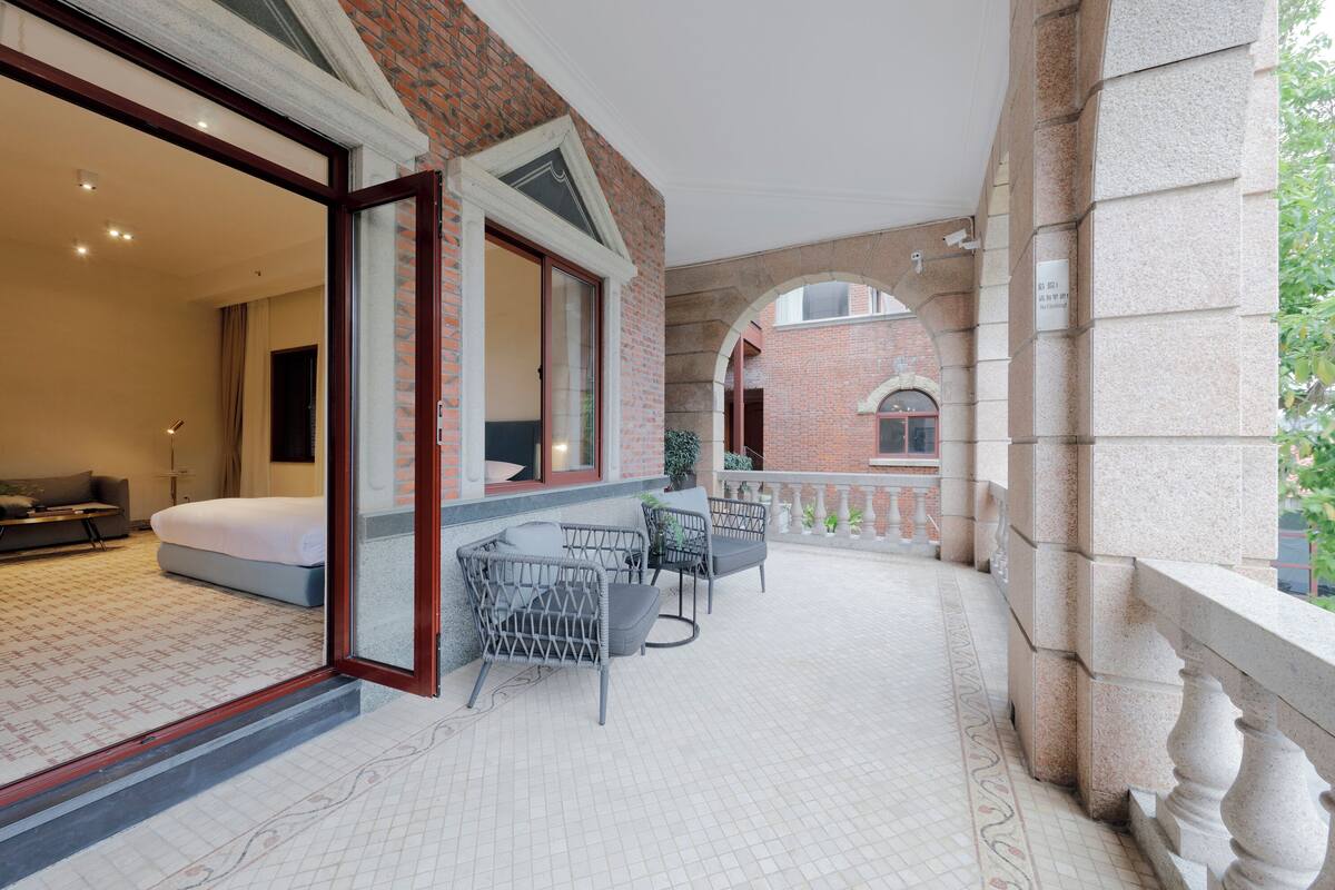 A hotel room with a bed, a sitting area with a sofa and a table, and a balcony with chairs.