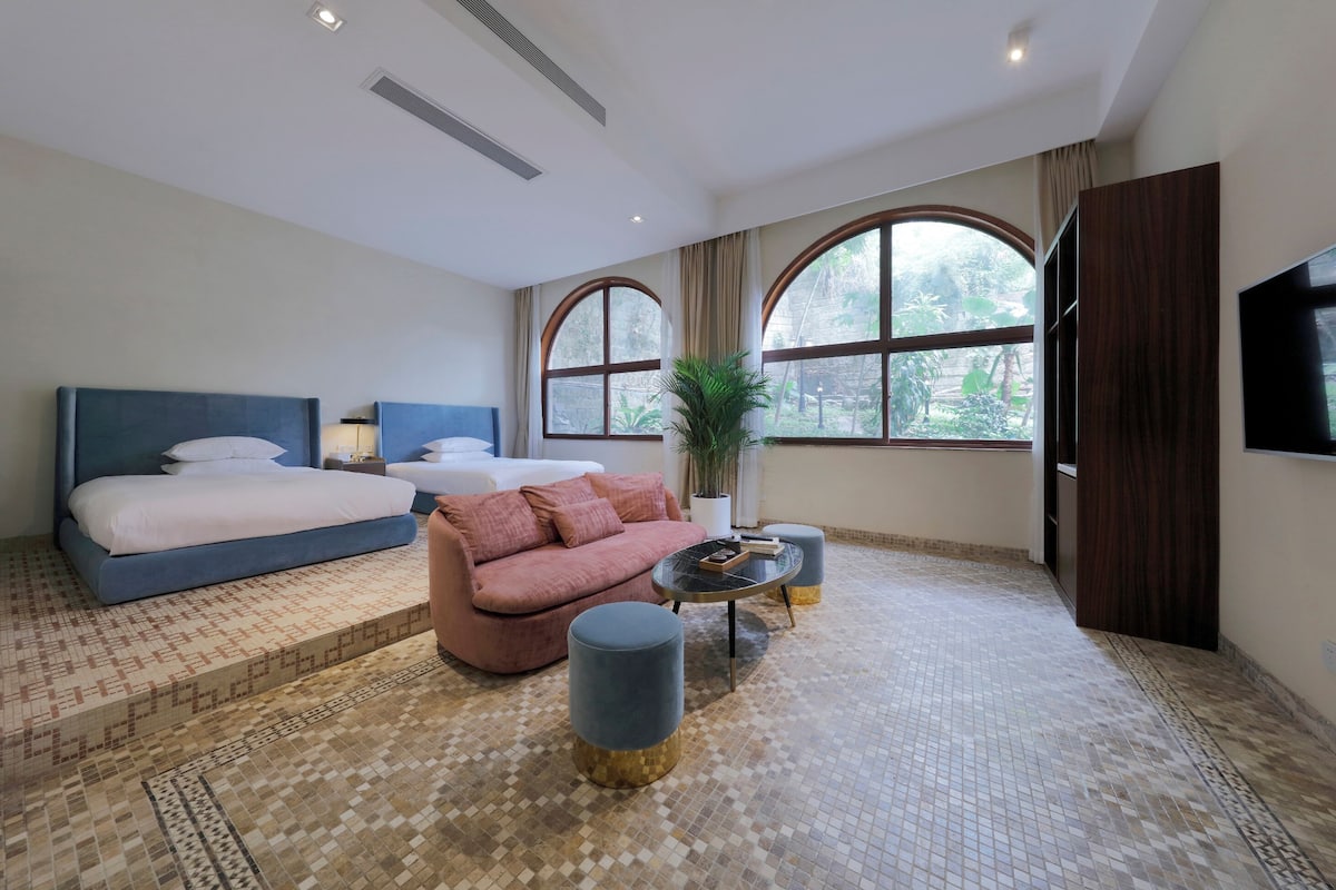 A modern hotel room with a large bed, a sofa, a coffee table, and a TV.