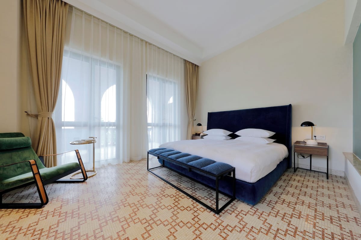 A hotel room with a large bed, a green armchair, a small table, and a lamp.